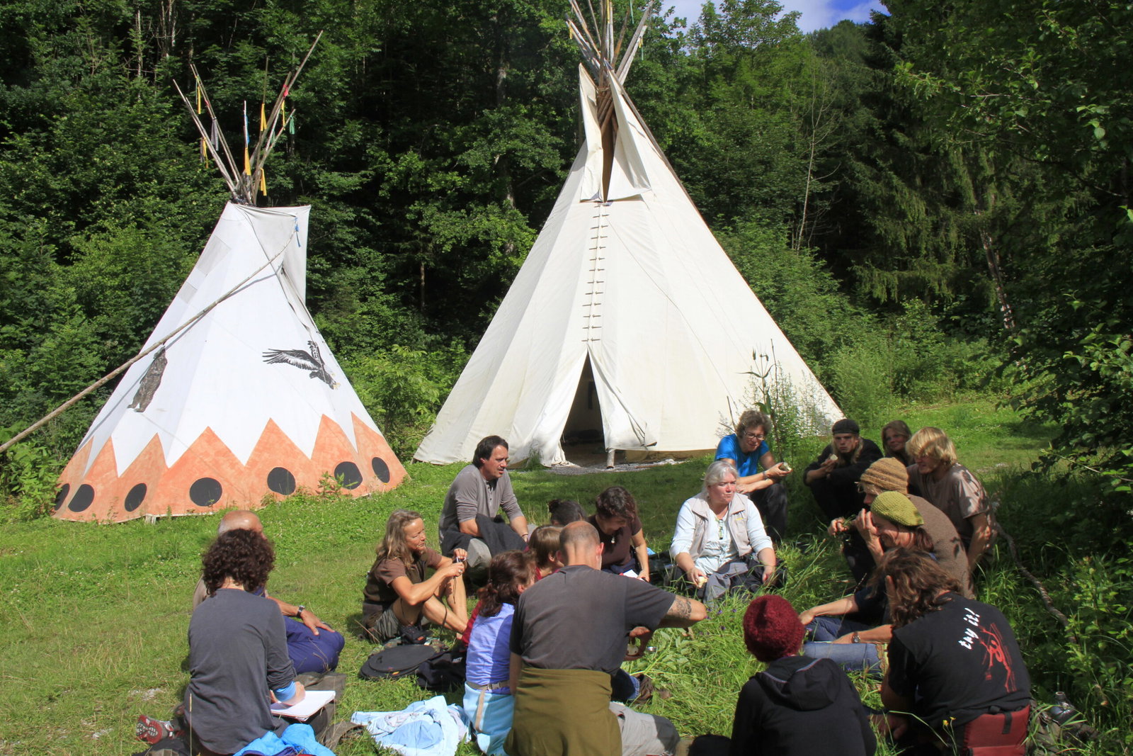 A group talking in front of two tipis at the edge of the forest